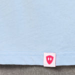 Close-up detail of a pink Double Diamond Shield woven hem label on a light blue long sleeve shirt.