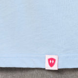 Close-up detail of a pink Double Diamond Shield woven hem label on a light blue long sleeve shirt.