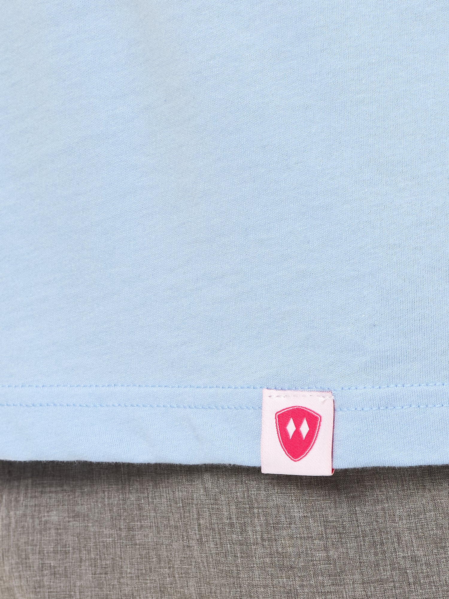 Close-up detail of a pink Double Diamond Shield woven hem label on a light blue long sleeve shirt.