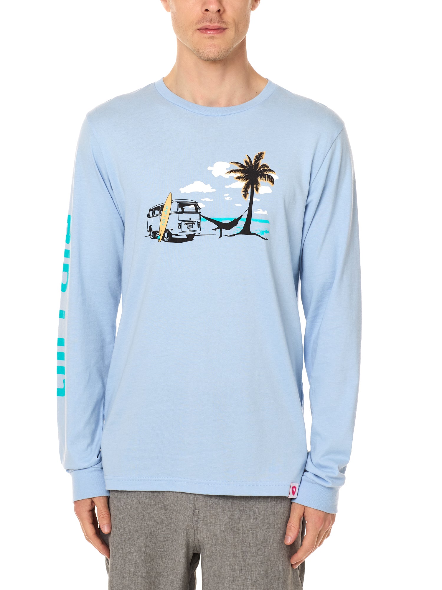 Front view of a male model wearing the Hammock long sleeve tee in light blue, displayed on a white background. The graphic depicts a vintage VW bus parked on a beach, with a surfboard leaning against it and a silhouetted figure relaxing in a hammock strung between the van and a palm tree.