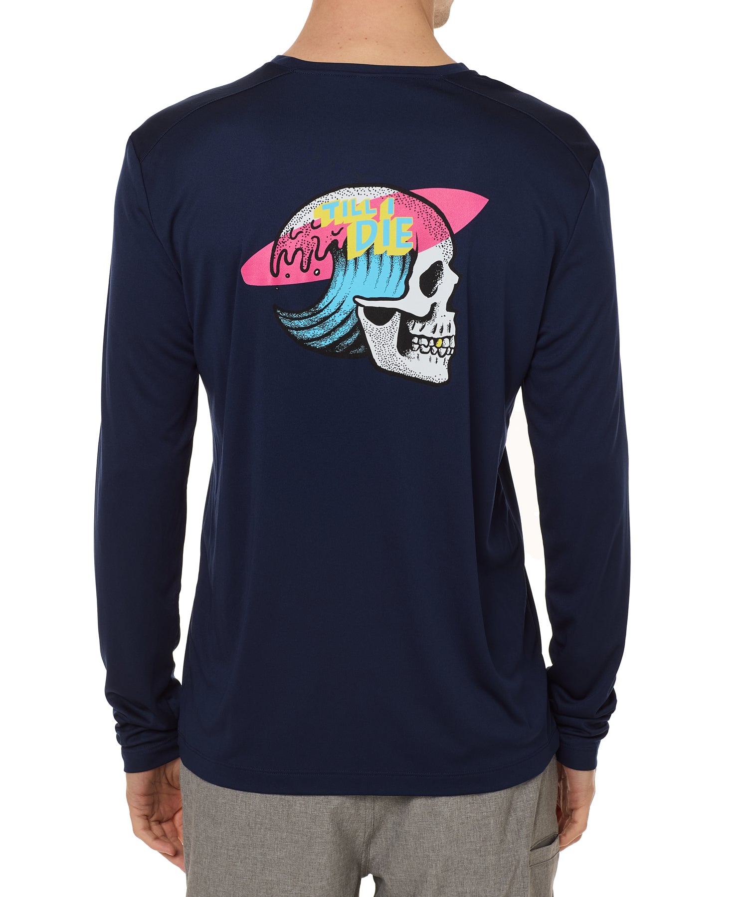 Back view of a male model wearing the Skull Wave Head performance long sleeve Tee in navy. The back graphic features a skull with a wave inside the head, overlapped by a pink surfboard and accented with yellow and blue "Till I Die" text.