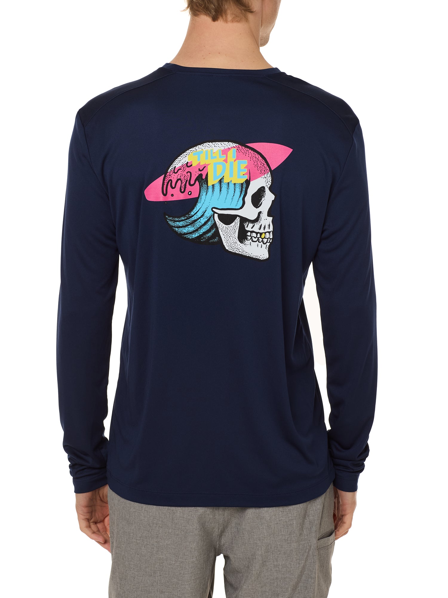 Back view of a male model wearing the Skull Wave Head performance long sleeve Tee in navy. The back graphic features a skull with a wave inside the head, overlapped by a pink surfboard and accented with yellow and blue "Till I Die" text.