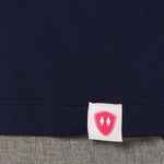 Close-up detail of a pink Double Diamond Shield woven hem label on a navy blue shirt.
