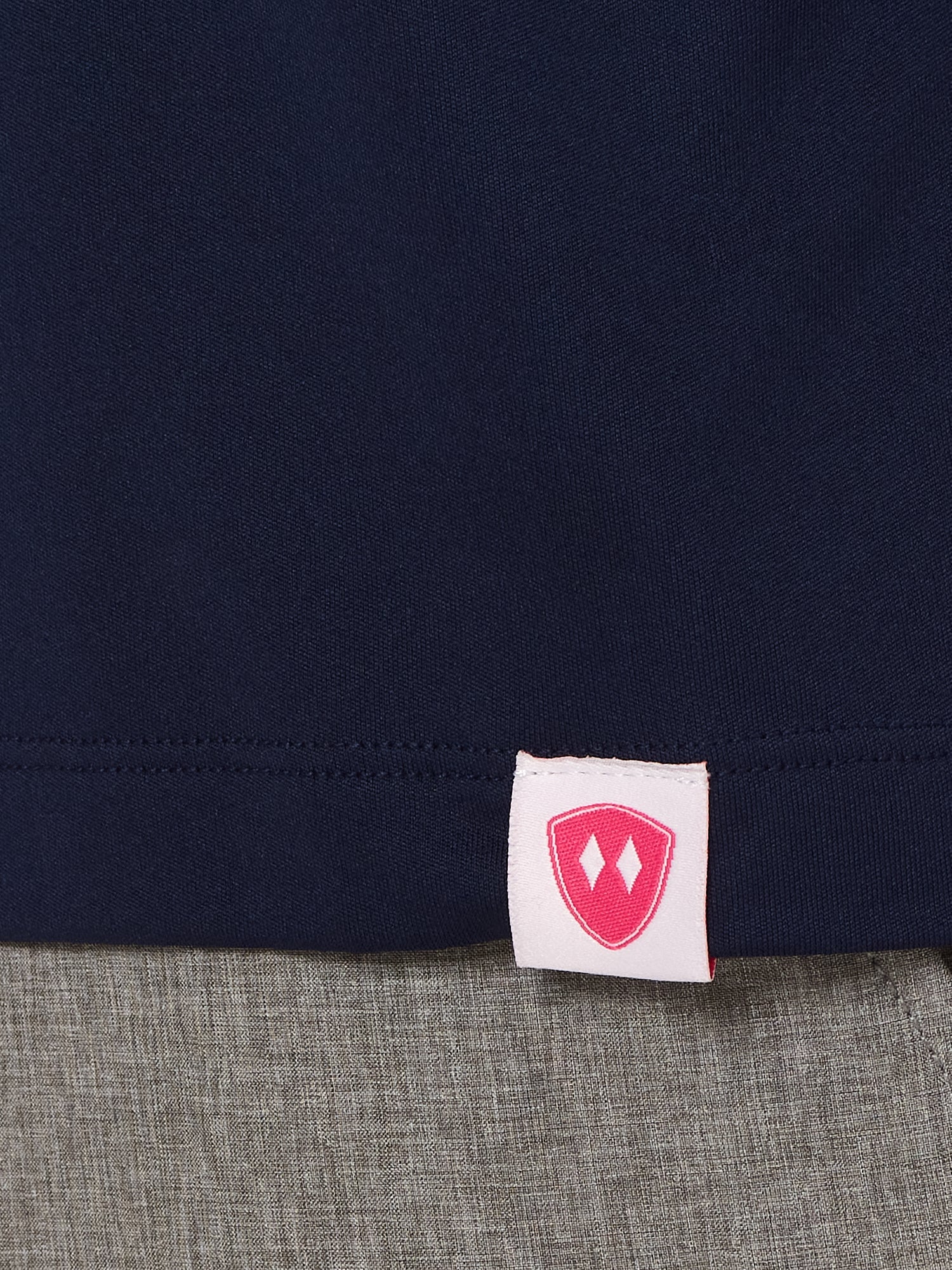 Close-up detail of a pink Double Diamond Shield woven hem label on a navy blue shirt.