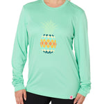 Front view of a female model wearing a mint green long sleeve performance shirt with a vibrantly colored retro pineapple graphic on the front.