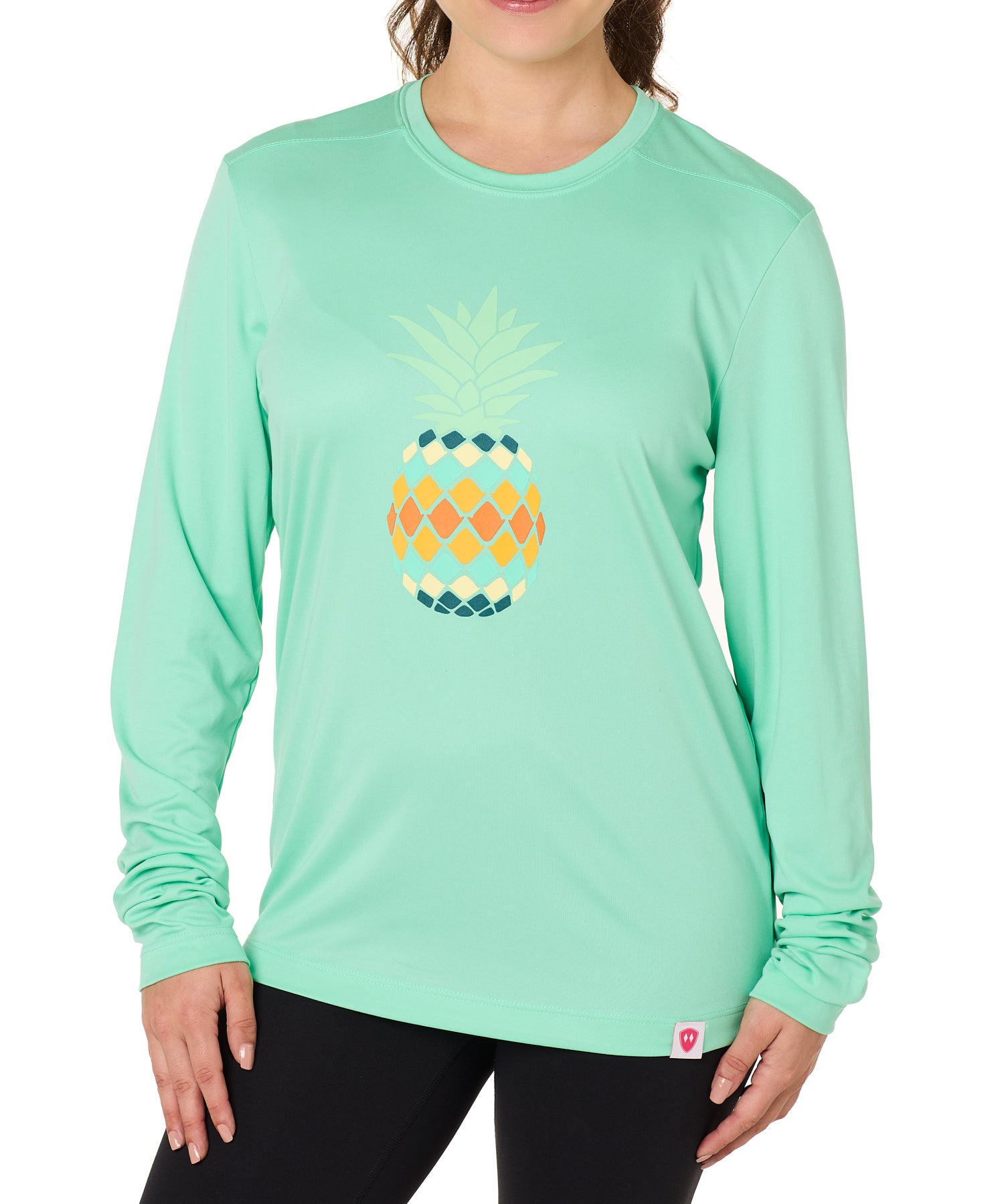 Front view of a female model wearing a mint green long sleeve performance shirt with a vibrantly colored retro pineapple graphic on the front.