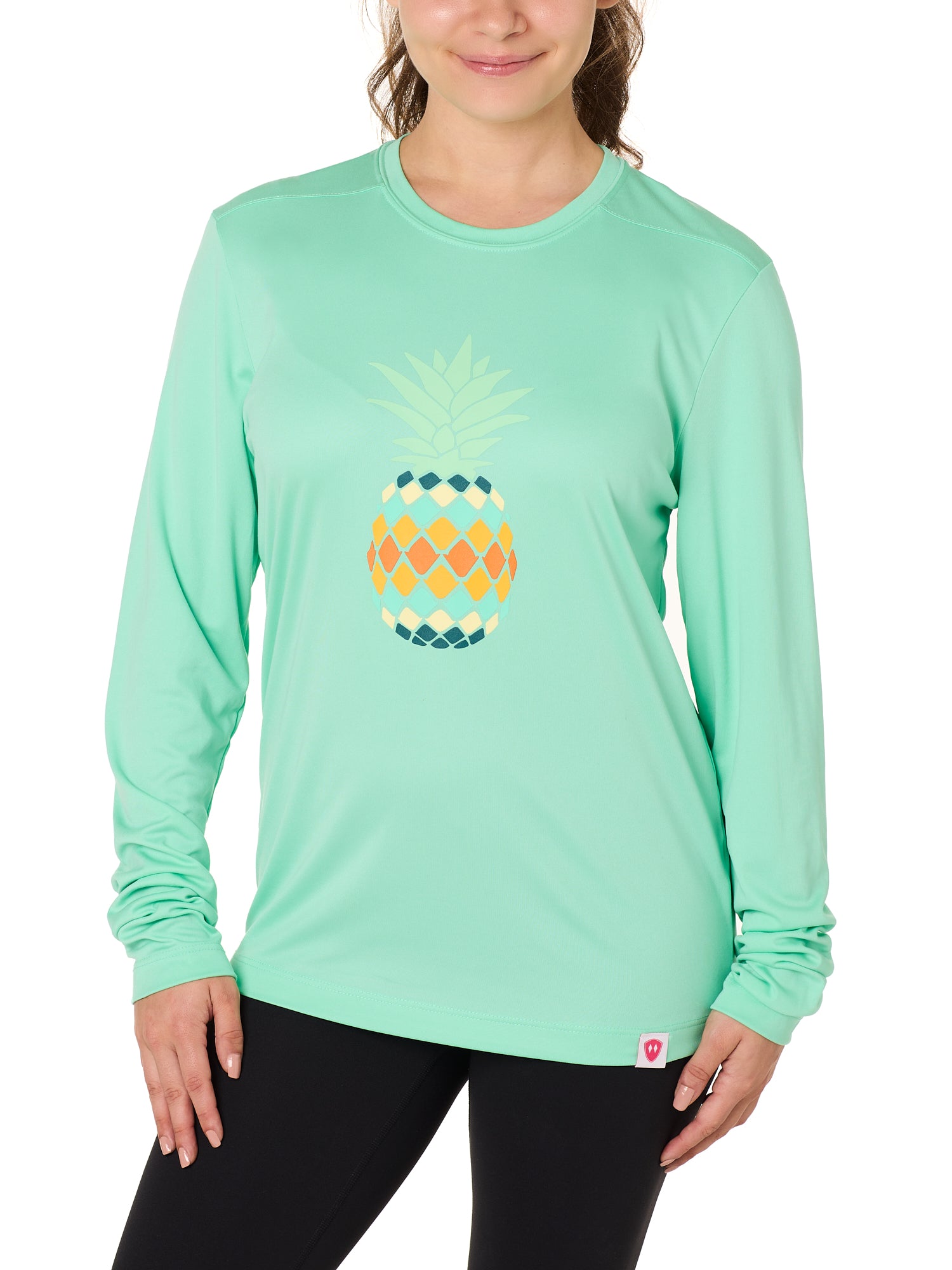 Front view of a female model wearing a mint green long sleeve performance shirt with a vibrantly colored retro pineapple graphic on the front.