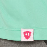 Close-up detail of a pink Double Diamond Shield woven hem label on a mint green performance long sleeve shirt.