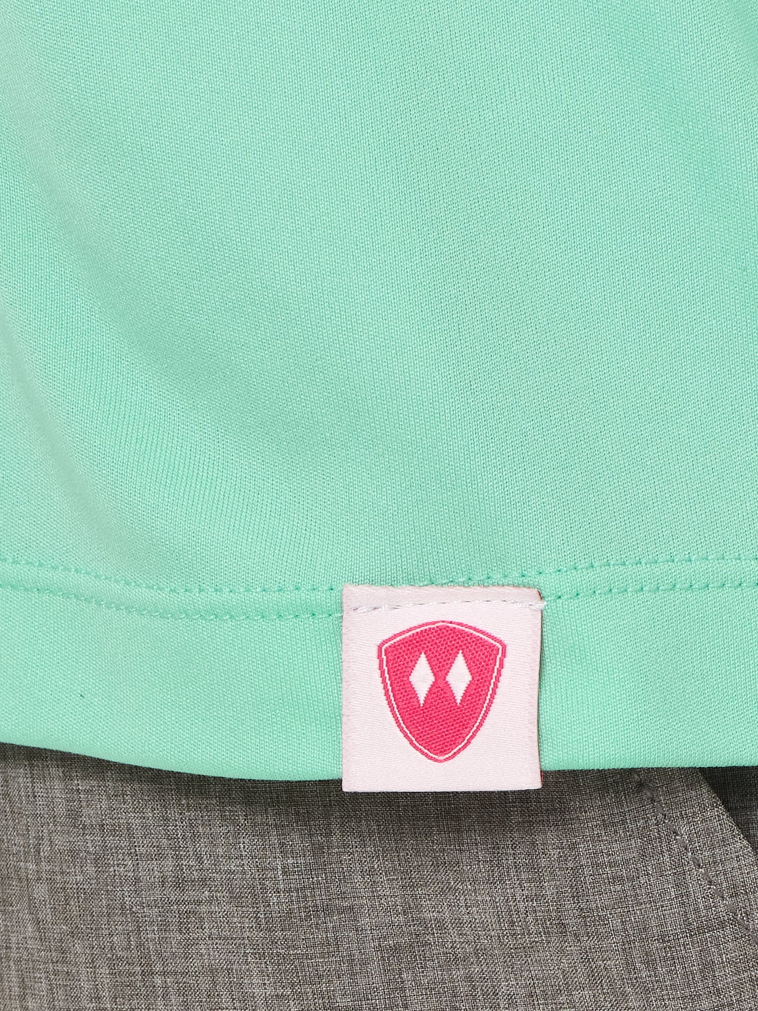 Close-up detail of a pink Double Diamond Shield woven hem label on a mint green performance long sleeve shirt.