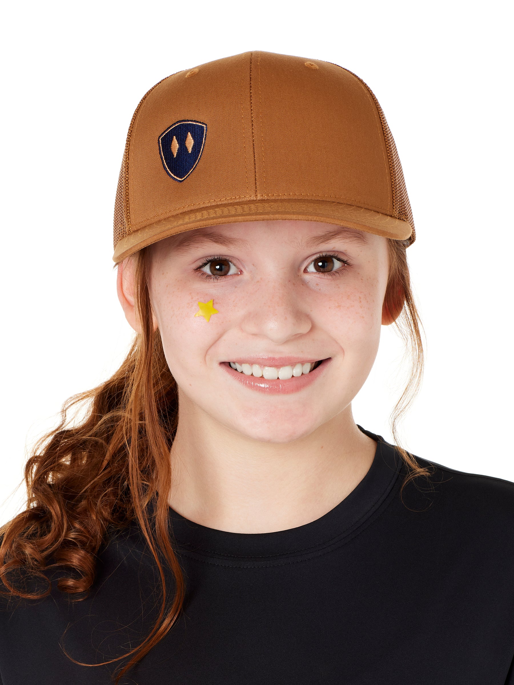 Front view of a youth wearing a caramel classic trucker hat with a navy blue embroidered double diamond shield on the bottom right panel
