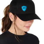 Front view of a female wearing a black classic trucker hat with a blue embroidered double diamond shield on the bottom right panel