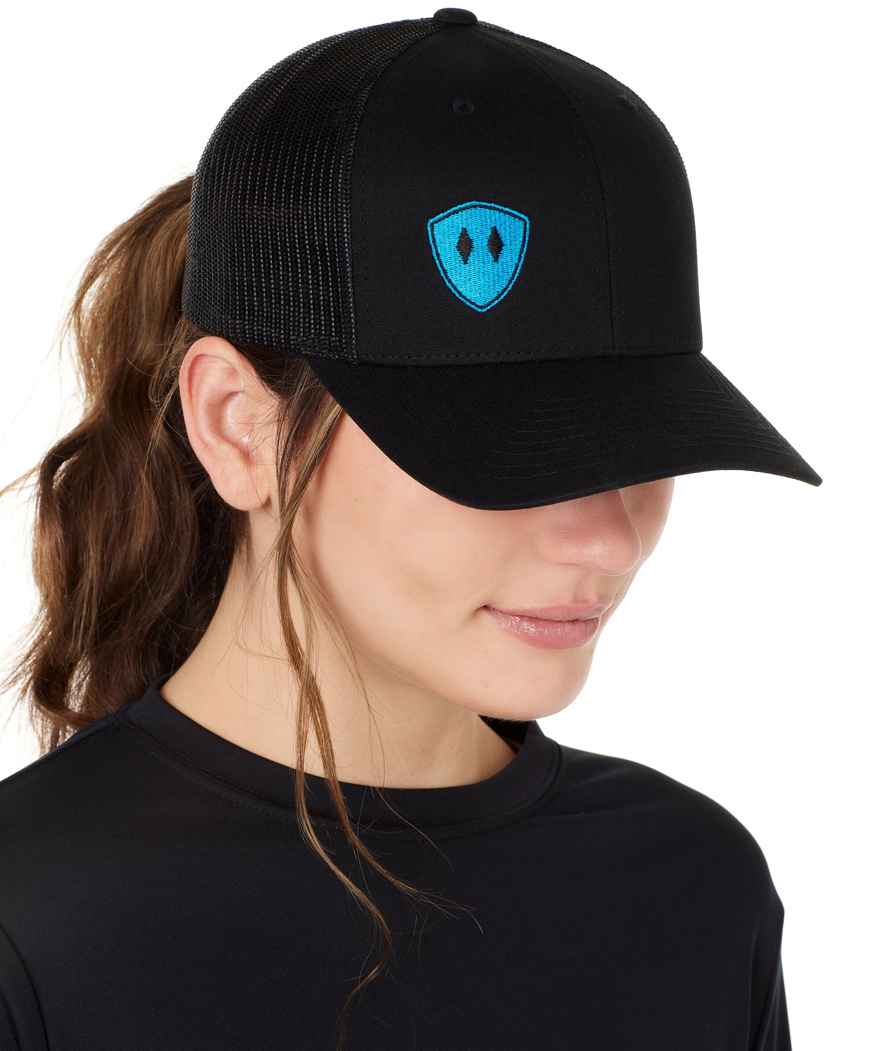 Front view of a female wearing a black classic trucker hat with a blue embroidered double diamond shield on the bottom right panel