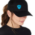 Front view of a female wearing a black classic trucker hat with a blue embroidered double diamond shield on the bottom right panel
