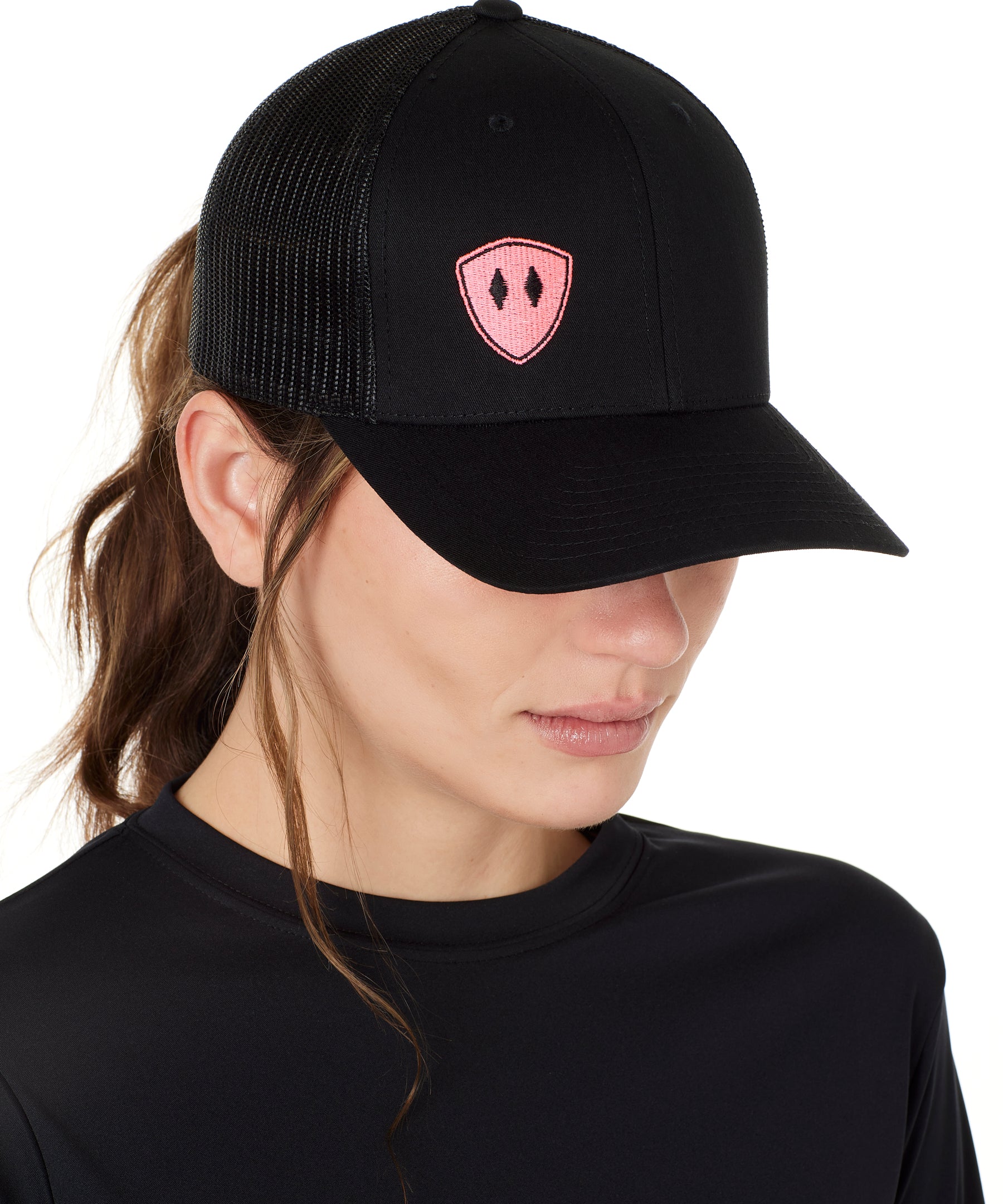 Front view of a female wearing a black classic trucker hat with a pink embroidered double diamond shield on the bottom right panel