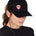 Front view of a female wearing a black classic trucker hat with a pink embroidered double diamond shield on the bottom right panel