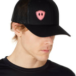 Front view of a male wearing a black classic trucker hat with a pink embroidered double diamond shield on the bottom right panel