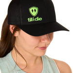 Front view of a female model wearing a black classic trucker hat, featuring a lime green embroidered Till I Die logo on the lower right front panel.