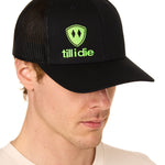 Front view of a male model wearing a black classic trucker hat, featuring a lime green embroidered Till I Die logo on the lower right front panel.