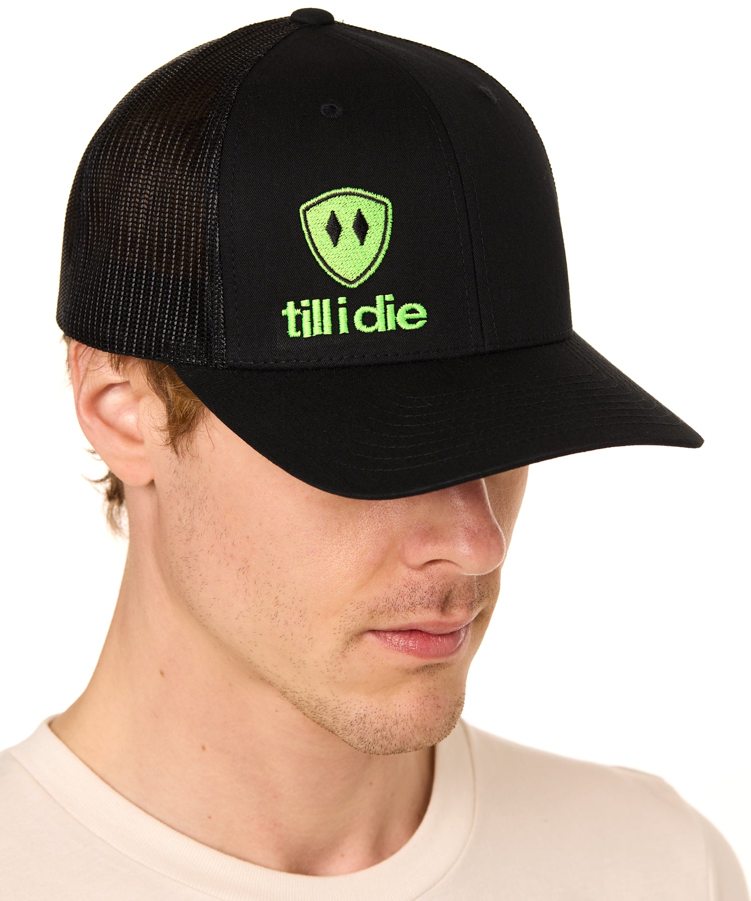 Front view of a male model wearing a black classic trucker hat, featuring a lime green embroidered Till I Die logo on the lower right front panel.