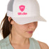 Front view of a female model wearing a white classic trucker hat, featuring a hot pink embroidered Till I Die logo on the lower right front panel.