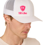Front view of a male model wearing a white classic trucker hat, featuring a hot pink embroidered Till I Die logo on the lower right front panel.