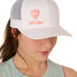 Front view of a female model wearing a white classic trucker hat, featuring a coral embroidered Till I Die logo on the lower right front panel.