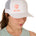 Front view of a female model wearing a white classic trucker hat, featuring a coral embroidered Till I Die logo on the lower right front panel.