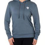 Front view of a female model wearing the Summer night hoodie in washed denim on a white background. The hoodie is embroider with a gray and white  double diamond shield over the wearers left chest.