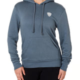 Front view of a female model wearing the Summer night hoodie in washed denim on a white background. The hoodie is embroider with a gray and white  double diamond shield over the wearers left chest.