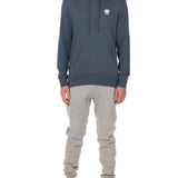 Front view of a male model wearing the Summer night hoodie in washed denim on a white background. The hoodie is embroider with a gray and white  double diamond shield over the wearers left chest. Paired with The Summer Nights mens joggers.