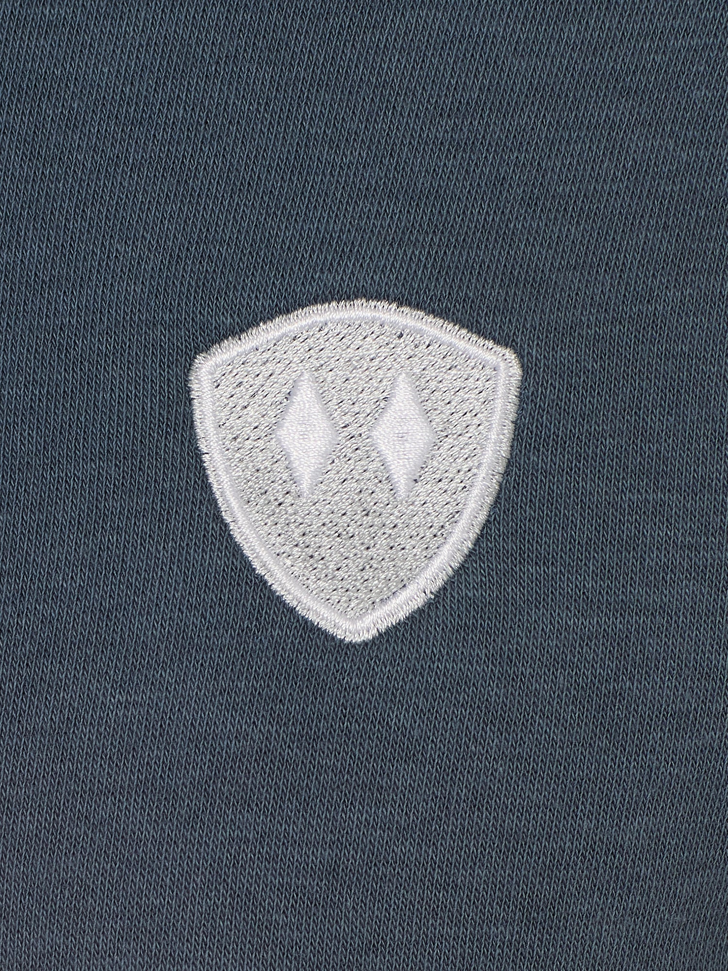 detail of a washed denim hoodie embroidered with a gray and white double diamond shield