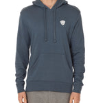 Front view of a male model wearing the Summer night hoodie in washed denim on a white background. The hoodie is embroider with a gray and white  double diamond shield over the wearers left chest.