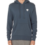 Front view of a male model wearing the Summer night hoodie in washed denim on a white background. The hoodie is embroider with a gray and white  double diamond shield over the wearers left chest.