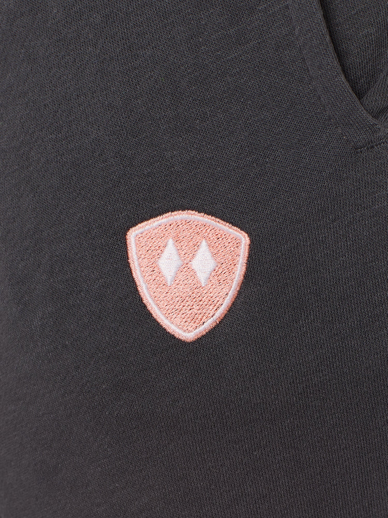 detail of a charcoal jogger embroidered with a coral and white double diamond shield