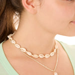 Close-up view of a female model wearing the Cream Outer Banks Cowrie necklace layered with the ivory Beachcomber’s Jewel necklace.