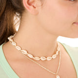 Close-up view of a female model wearing the Cream Outer Banks Cowrie necklace layered with the ivory Beachcomber’s Jewel necklace.