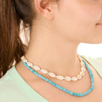 Close-up view of a female model wearing the blue Echoes of Atlantis necklace layered with the turquoise Outer Banks Cowrie necklace.