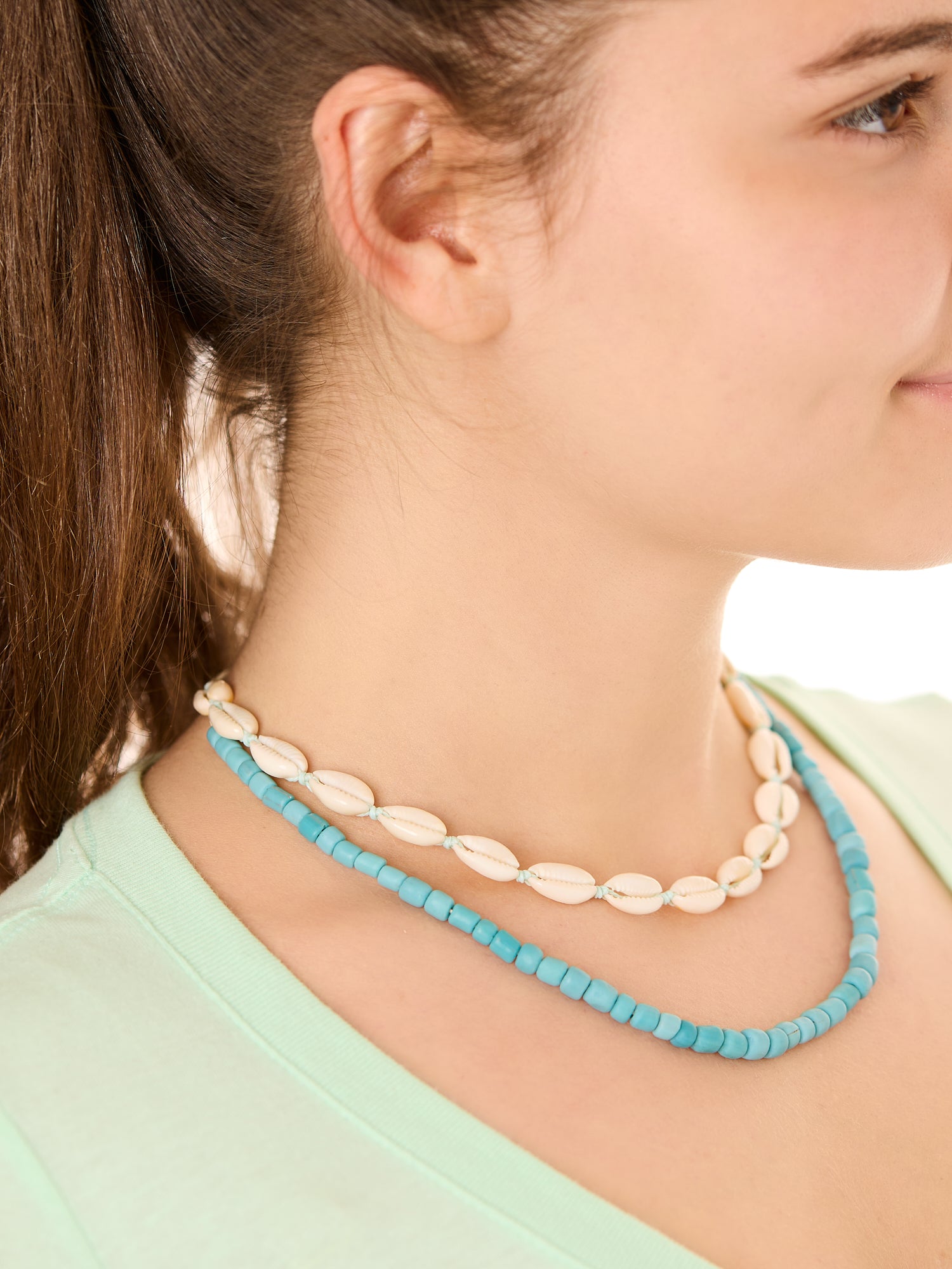 Close-up view of a female model wearing the blue Echoes of Atlantis necklace layered with the turquoise Outer Banks Cowrie necklace.