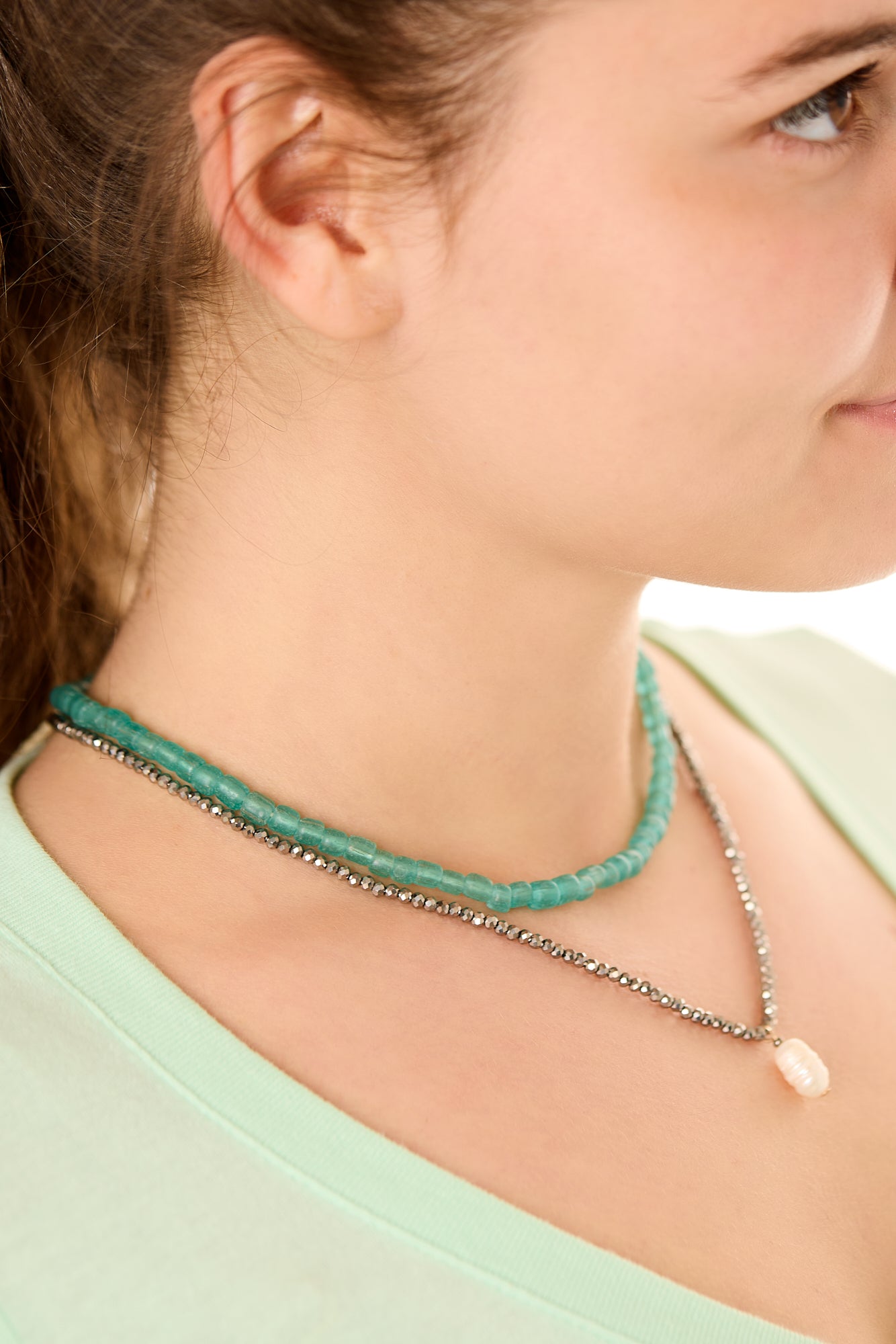Close-up view of a female model wearing the green Echoes of Atlantis necklace layered with the gray Beachcomber’s Jewel necklace.