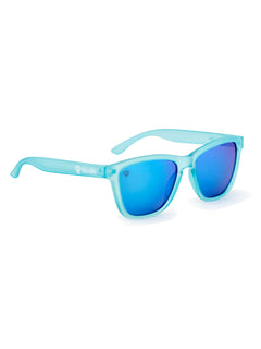 Front view of the Blue Mirage sunglasses on a white background. The light blue frosted translucent PVC frames are accented with a white Till I Die logo on the arm. The lenses are medium blue, with the right lens featuring an etched Double Diamond Shield in the top right corner.