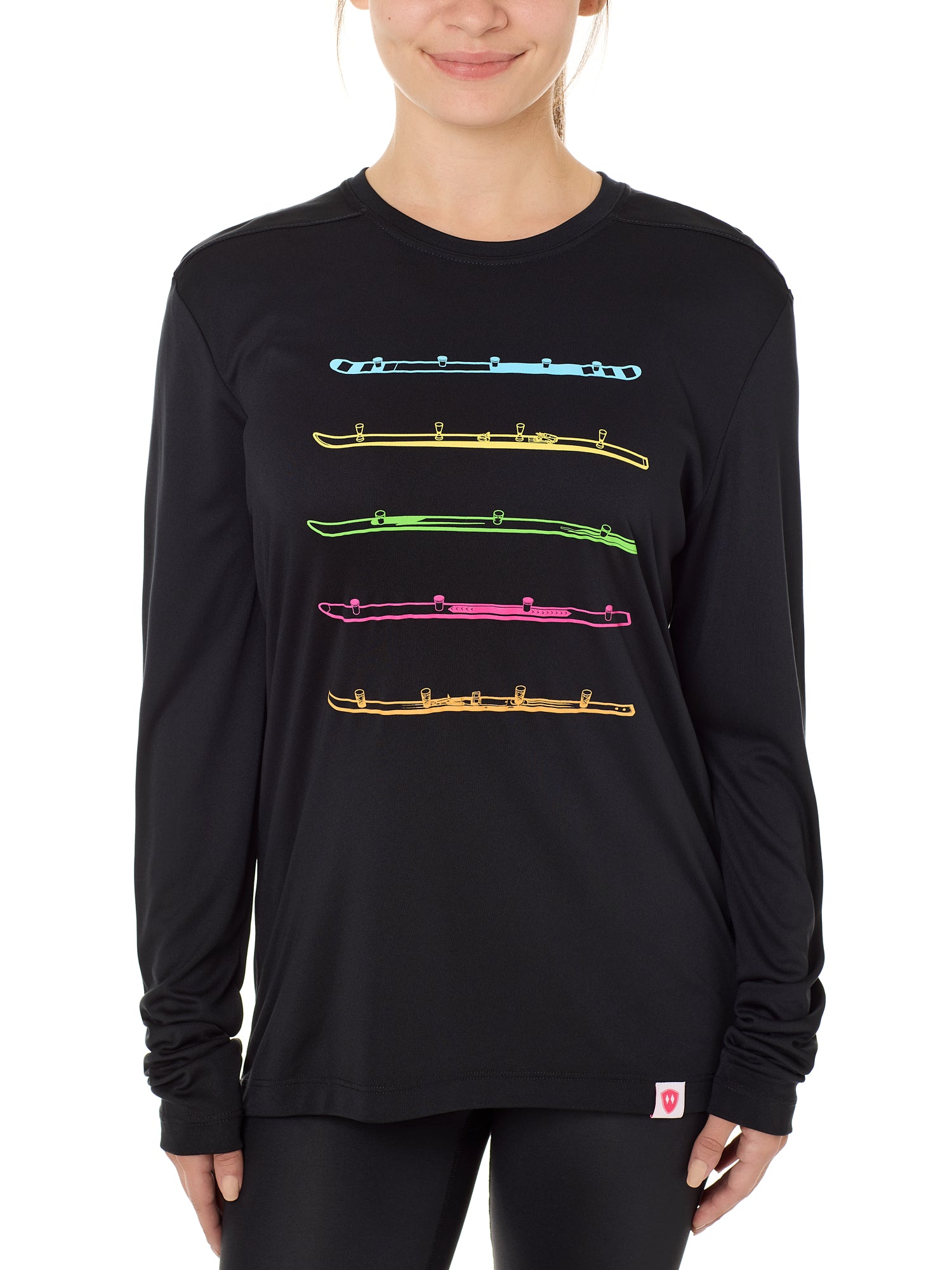 Front view of a female model wearing the black Shot Ski performance long sleeve shirt on a white background. Graphic features five multicolored shot skis illustrated in a line art style across the front.