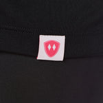 Close-up detail of a pink Double Diamond Shield woven hem label on a black performance long sleeve shirt.