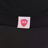 Close-up detail of a pink Double Diamond Shield woven hem label on a black performance long sleeve shirt.