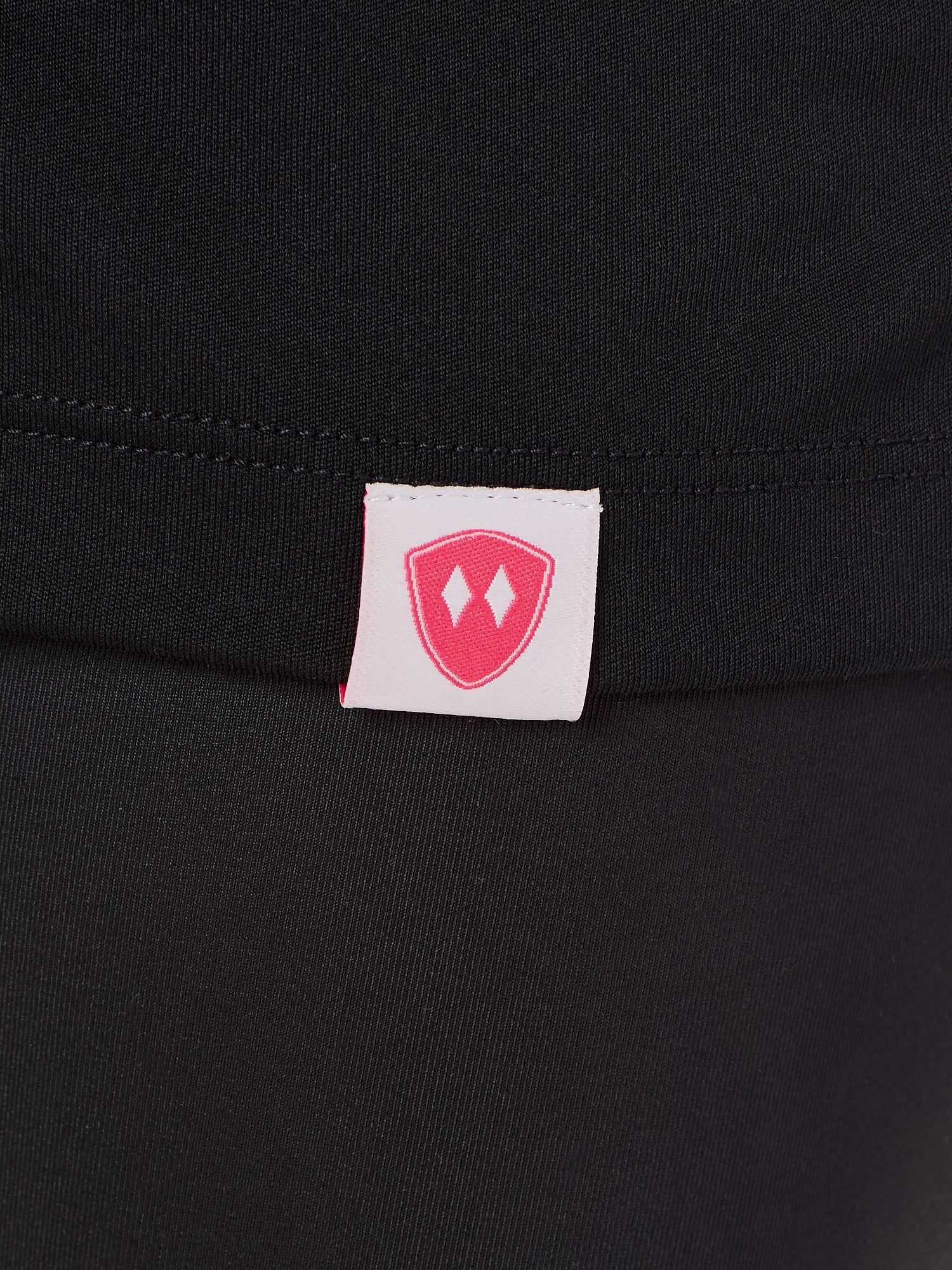 Close-up detail of a pink Double Diamond Shield woven hem label on a black performance long sleeve shirt.