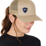A woman wearing a tan and navy one-size snapback trucker hat with a logo on the front.