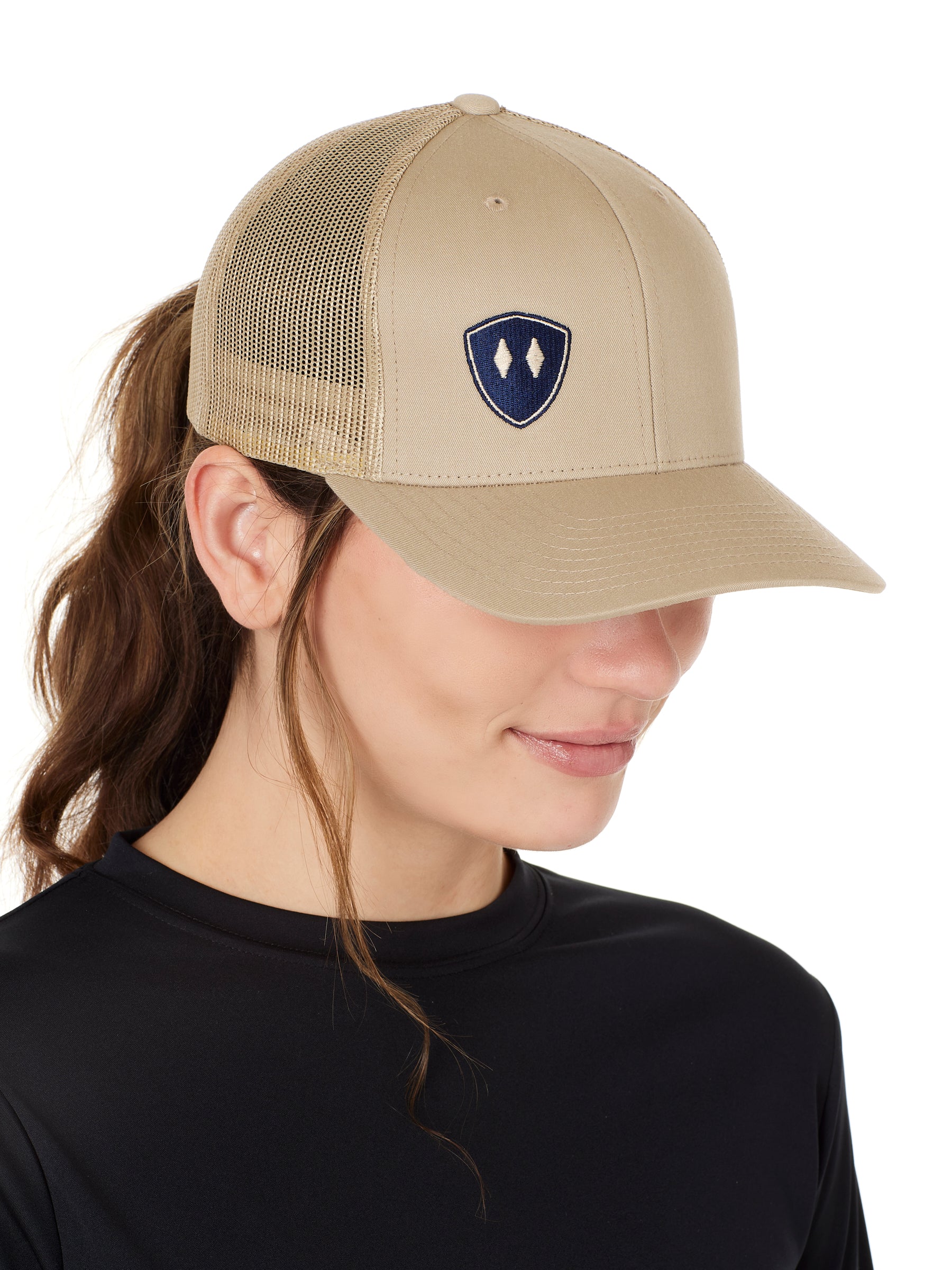 A woman wearing a tan and navy one-size snapback trucker hat with a logo on the front.