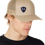 MAN WEARING A TAN TRUCKER HAT WITH NAVY DOUBLE DIAMOND SHIELD LOGO