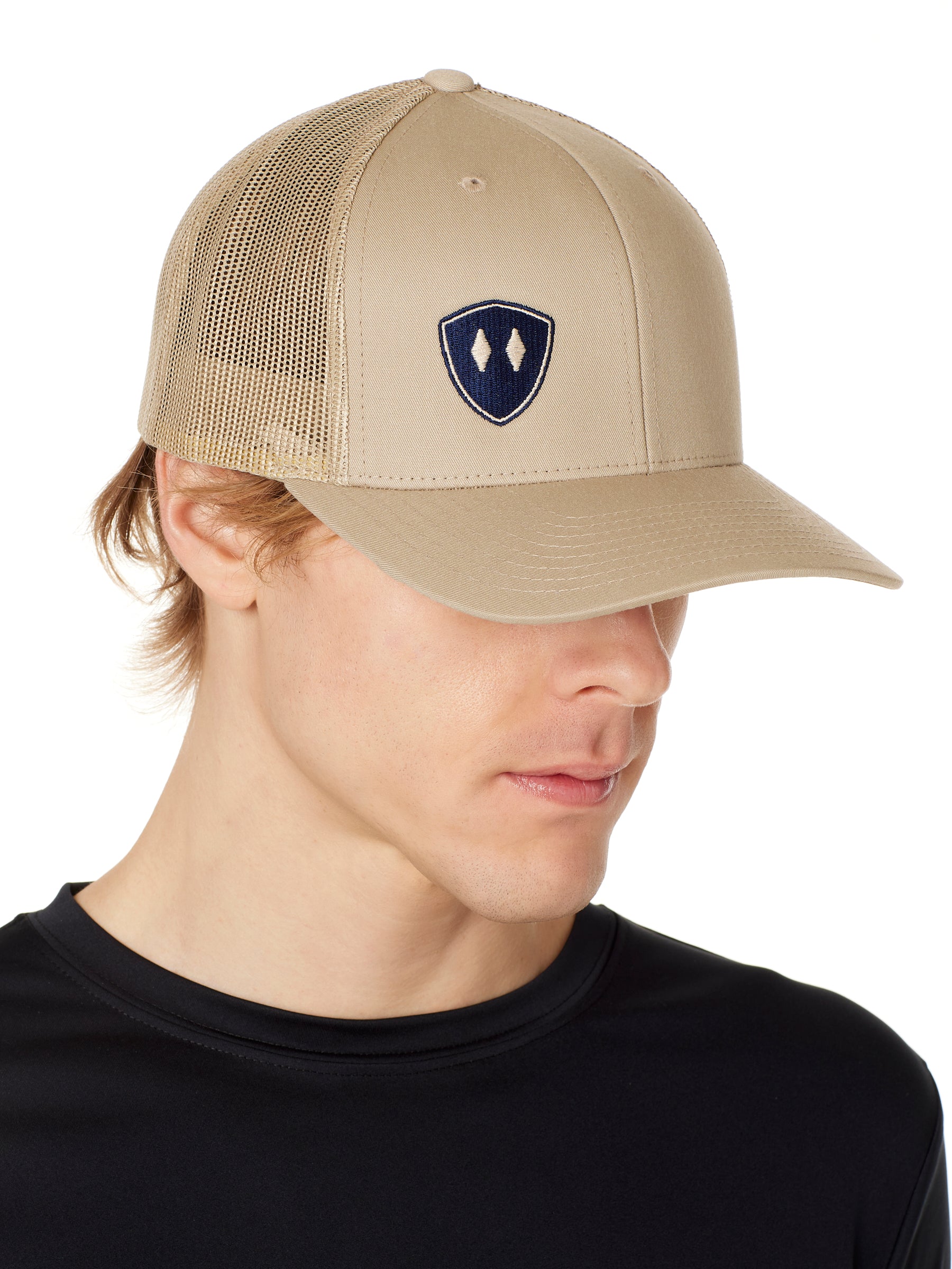 MAN WEARING A TAN TRUCKER HAT WITH NAVY DOUBLE DIAMOND SHIELD LOGO