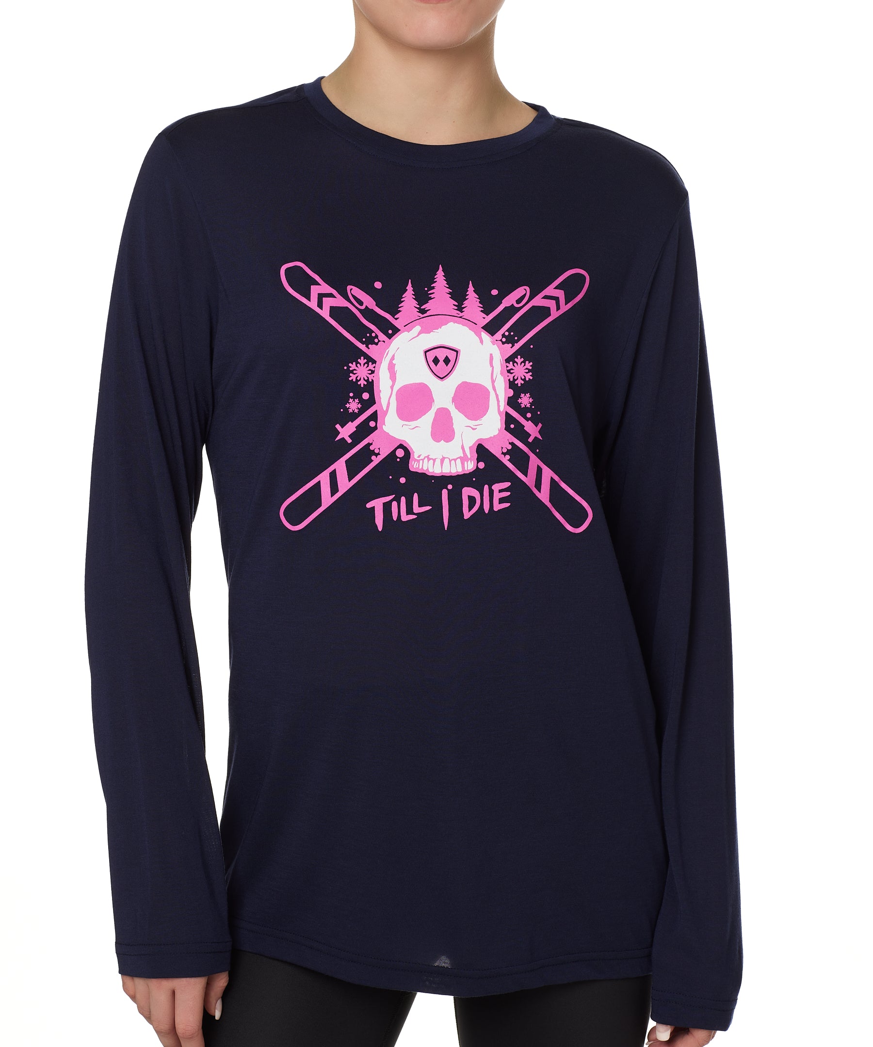 Front view of a female model wearing the ULLR navy crew neck long sleeve tee on a white background. The pink and white graphic features a skull over crossed skis, with snowflakes, pine trees, and “Till I Die” text layered below.