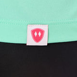 Close-up detail of a pink Double Diamond Shield woven hem label on a mint green performance long sleeve shirt.
